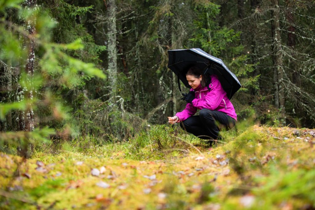 Jessica sätter sig på huk i skogen under ett paraply.