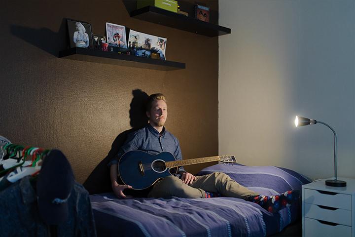 Tatu istuu sängyllään kädessään kitara. 