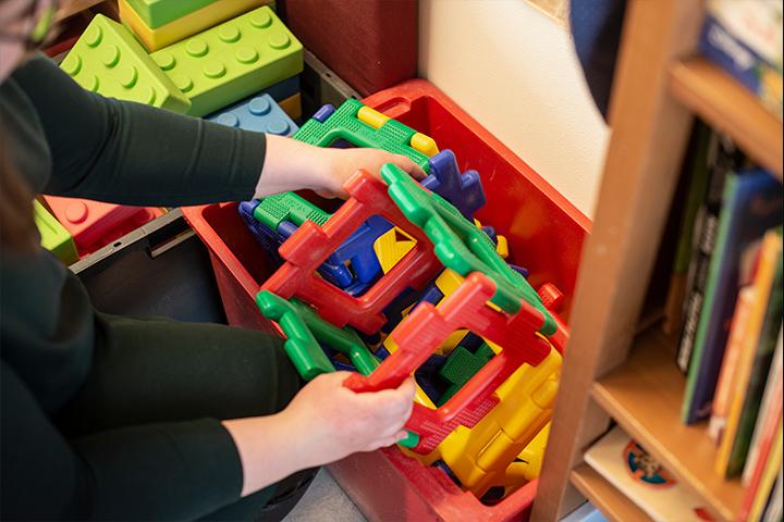 Heidi tar en stor och färgglad plastleksak från en leksakslåda.