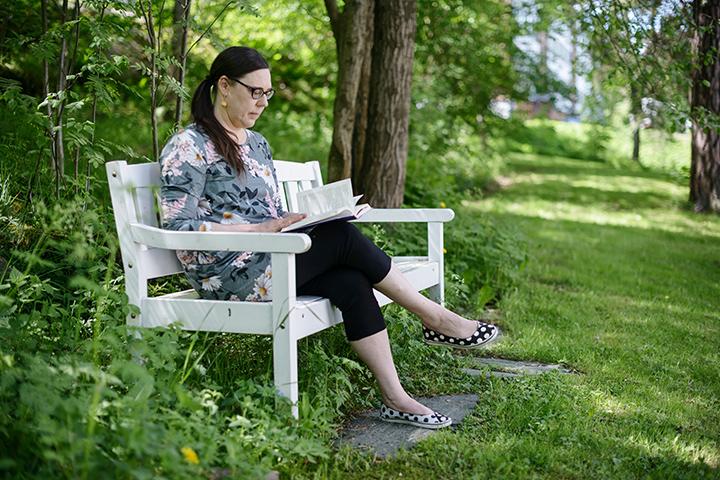 Katja Jokiniemi läser en bok på en parkbänk.