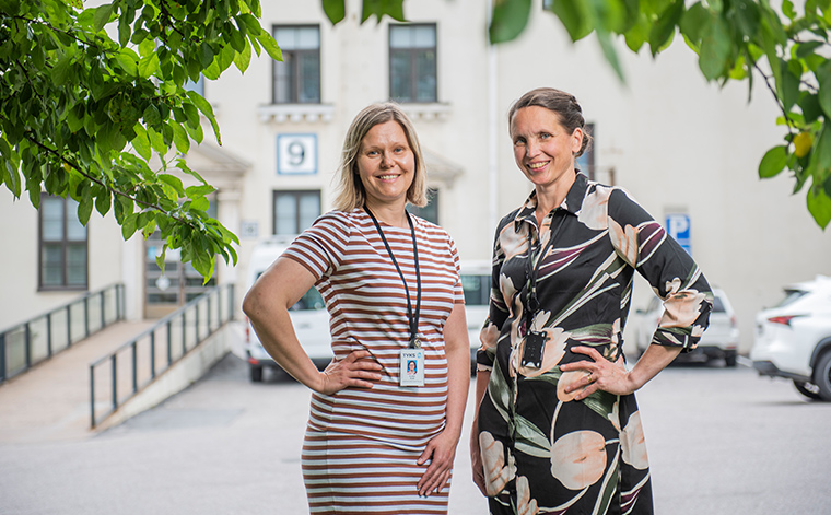 Elina Alm ja Jaana Häyrinen seisovat ulkona sairaalan edessä hymyillen kameraan.