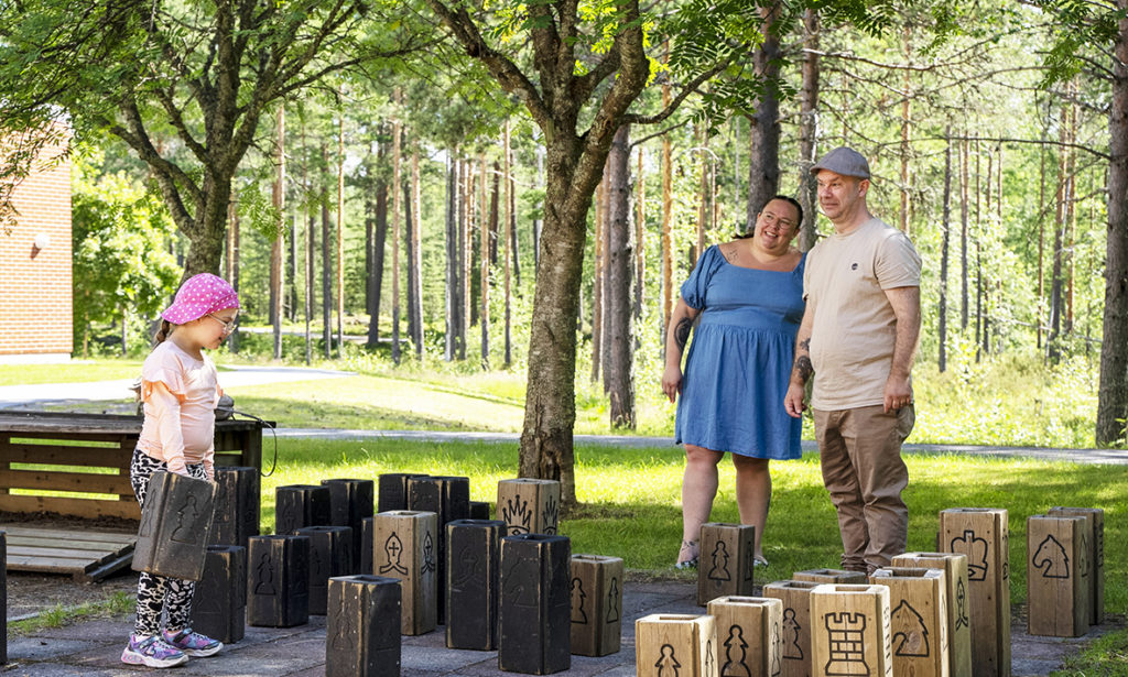 Säde, Sanna och Marko står på ett stort schackbräde på kurscentrets gård. 