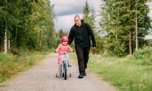 Jani går bredvid när dottern cyklar på sin cykel med stödhjul.