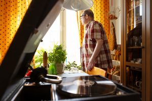 : I förgrunden syns en gammal grammofon. Jyrki står i bakgrunden och tittar ut genom fönstret.