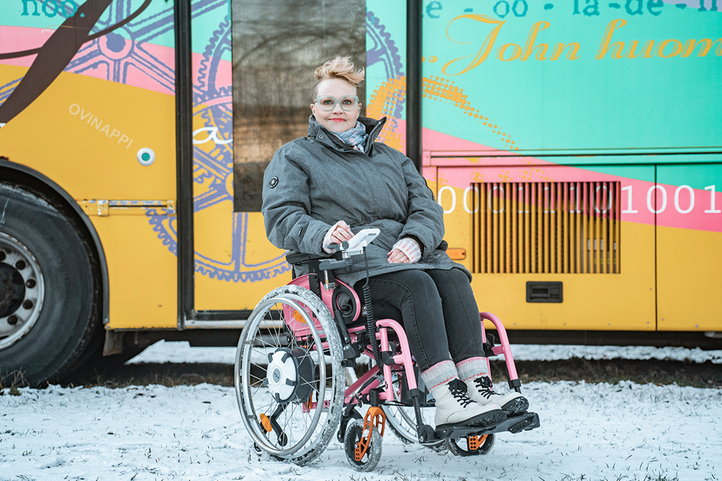 Riikka istuu sähköpyörätuolissa ulkona.