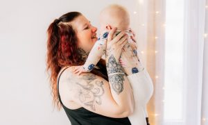 Jenni lyfter upp babyn och ler mot honom.