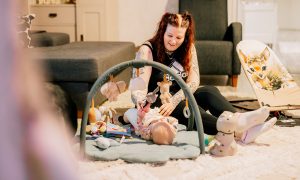 Babyn ligger på golvet under en aktiveringsleksak med Jenni intill.