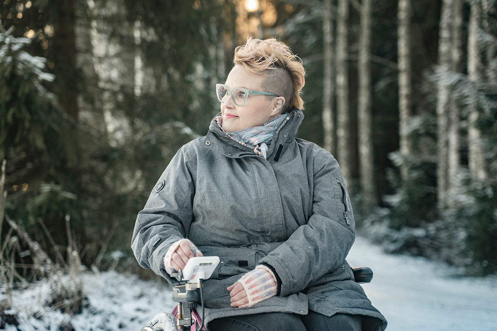 Riikka istuu sähköpyörätuolissa ulkona.