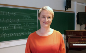 Iloinen musiikinopettaja liitutaulun edessä.