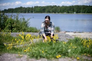 Katja on kyykistyneenä rantakalliolla ja katselee kukkia.
