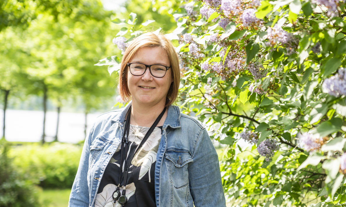 Taru Pellikainen, chef för utkomststödsteamet, står utomhus bredvid en syrenbuske.