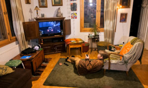 Sakke makoilee olohuoneen lattialla pää nojatuoliin nojaten ja pelaa videopeliä.
