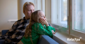 Lapsi ja vanhempi istuvat sohvalla ja lapsi katselee ikkunasta ulos.