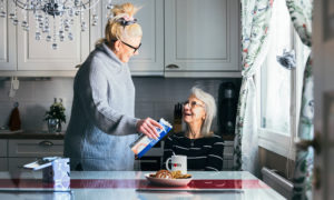 Marika kaataa Ainon kahvimukiin maitoa. Mukissa on teksti mom eli äiti.