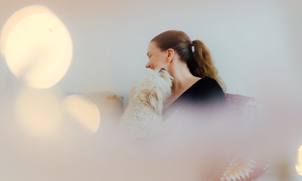 Laura sitter med en lurvig hund i famnen som snusar henne på kinden. 