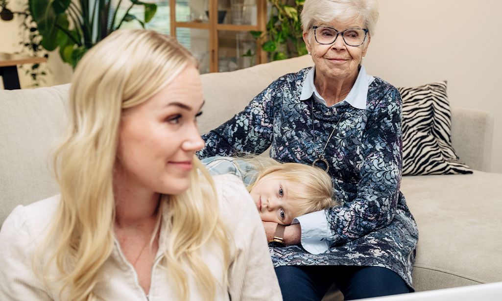 Iida Latva och Paula Lehtinen sitter i soffan. Iidas son ligger i gammelmormors famn. 