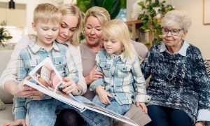 Iida Latva, Maija Latva och Paula Lehtinen sitter i soffan. Iidas söner sitter i Iidas och Maijas famn. De lyssnar på en saga.