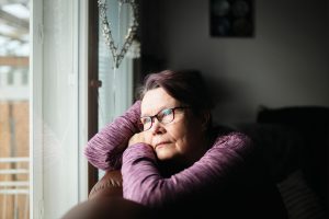 Rauni sitter i soffan, lutar sig mot händerna och tittar ut genom fönstret.