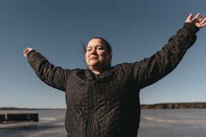 Hanne står utomhus med ögonen stängda och armarna utsträckta.