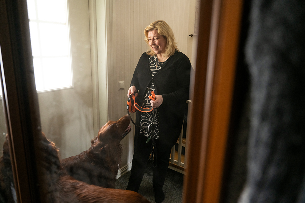 Sanna ska ta en promenad med sin hund. Sanna har hundens koppel i handen, hunden väntar framför henne.