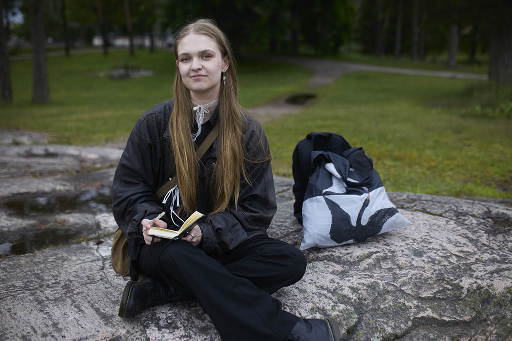 Enni sitter utomhus och ritar i ett anteckningshäfte.
