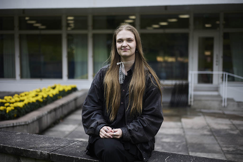 Enni sitter på stenbeläggningen och tittar in i kameran.