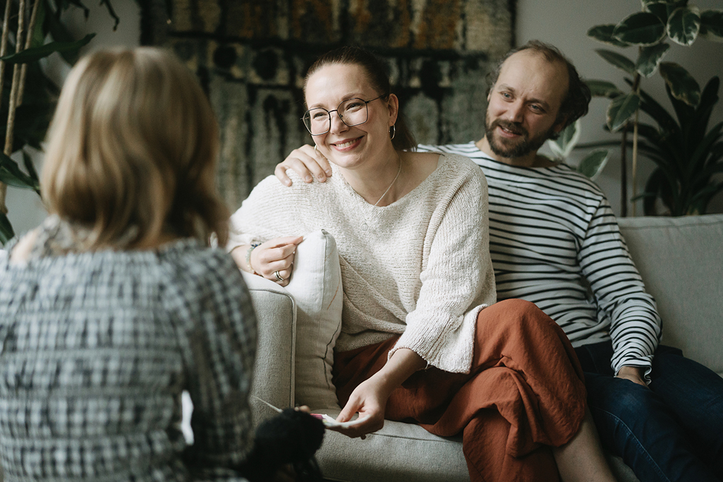 Katri och Akseli sitter bredvid varandra i soffan och pratar med Akselis dotter. 