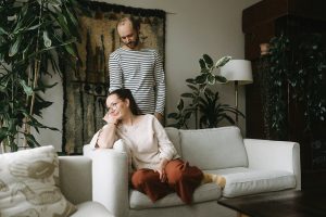 Katri Pentti sitter i soffan och hennes make Akseli Pentti står bakom henne. De håller varandra i handen.