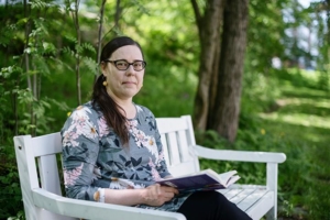 Katja Jokiniemi istuu puistonpenkillä kirja sylissä ja katsoo kameraan.