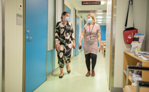 Jaana Häyrinen ja Elina Alm kävelevät sairaalan käytävällä kasvomaskit yllä ja katsovat toisiinsa.