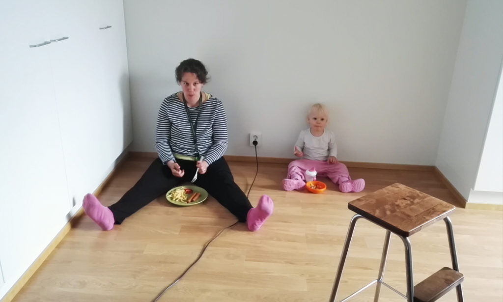 Suvi ja hänen tyttärensä istuvat lattialla ja syövät ruokaa keskellä muuttoa.