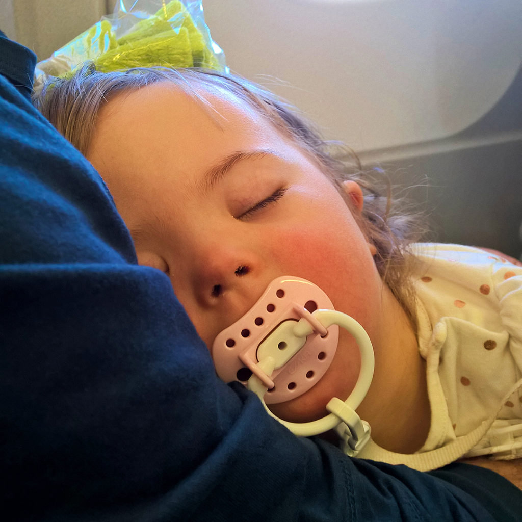 Säde nukkuu isän tai äidin sylissä lentokoneessa.