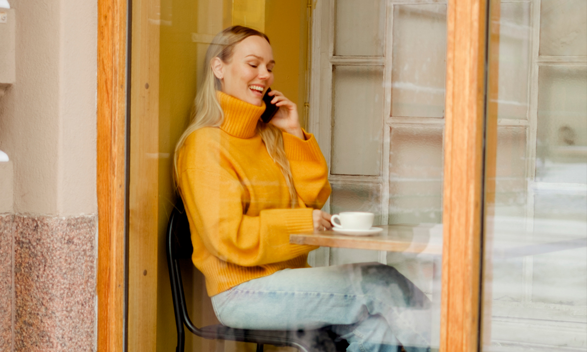 Nuori nainen kahvilassa puhumassa puhelimeen.