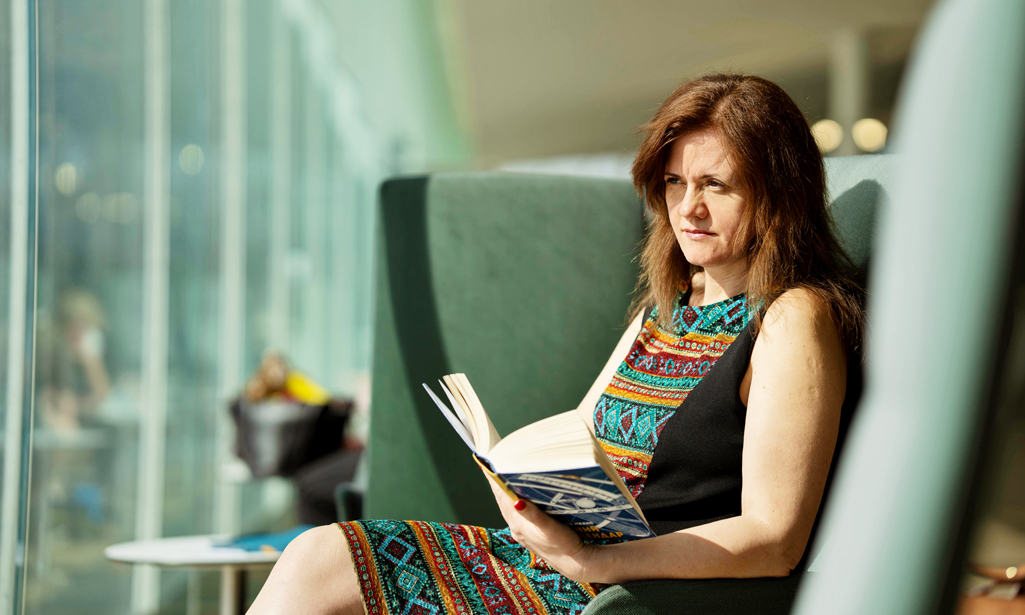 Oksana Horbanova sitter i en fåtölj i Helsingfors centrumbibliotek Ode och läser en bok.