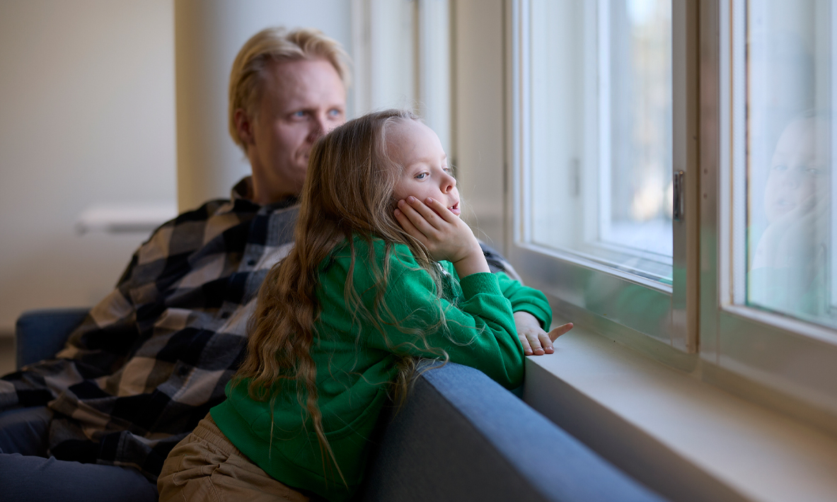 Lapsi ja vanhempi istuvat sohvalla ja lapsi katselee ikkunasta ulos.