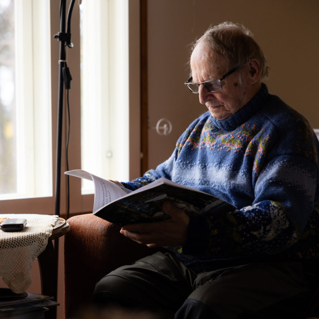 Henkilö istuu sohvalla ikkunan edessä ja lukee lehteä.