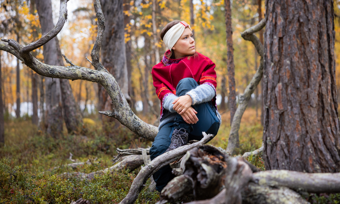 Henkilö istuu puun rungolla ruskan värittämässä metsässä.