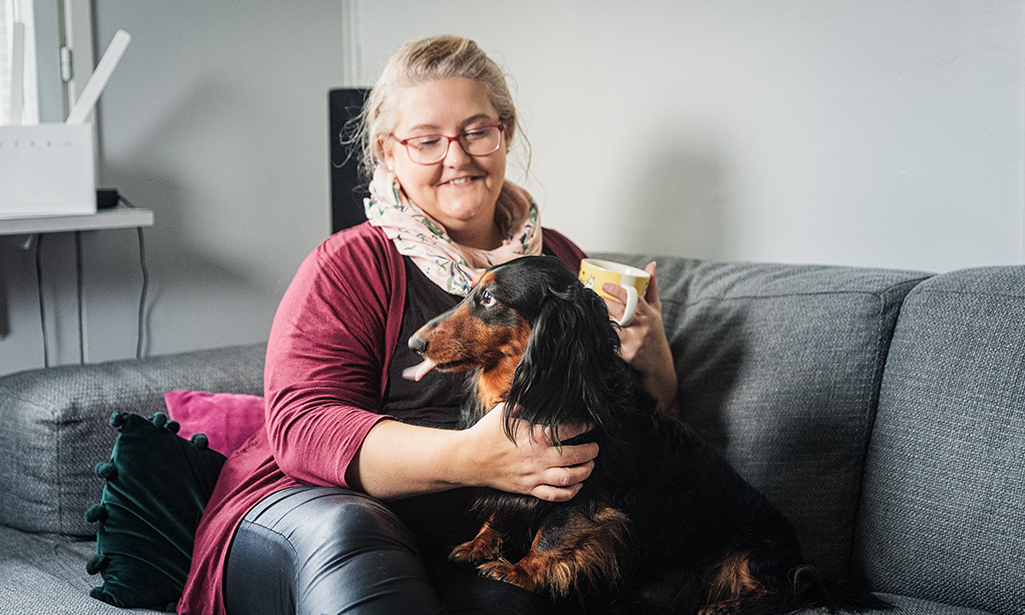 Sanna sitter i soffan och hunden sitter i hennes famn. 